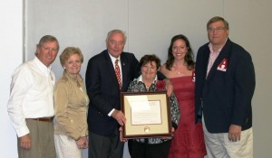 Group of people standing in room with white wall and lady in center holding plaque.