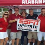 Group of people standing under red Alabama tent holding ESPN sign.