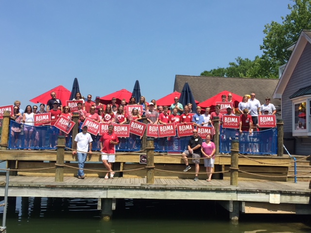 Group of people standing on pier holding red Bama signs.