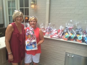 Two ladies standing outside in front of white brick wall holding a gift basket.