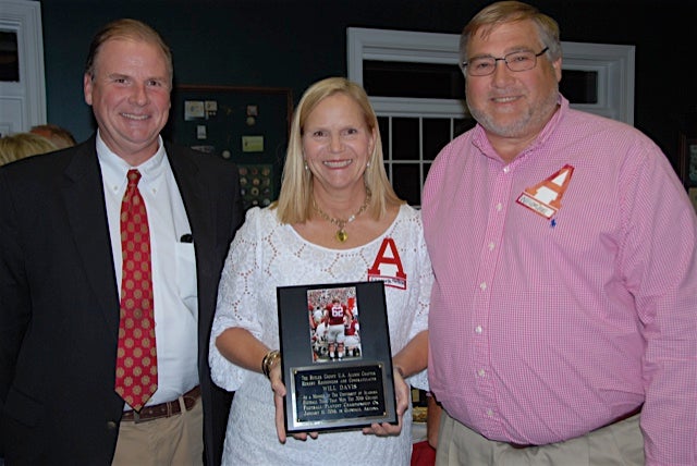 Three people standing and lady in middle holding plaque in dim light room.