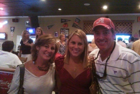 Man in black shirt and to women in red shirts sitting in front of dark wall