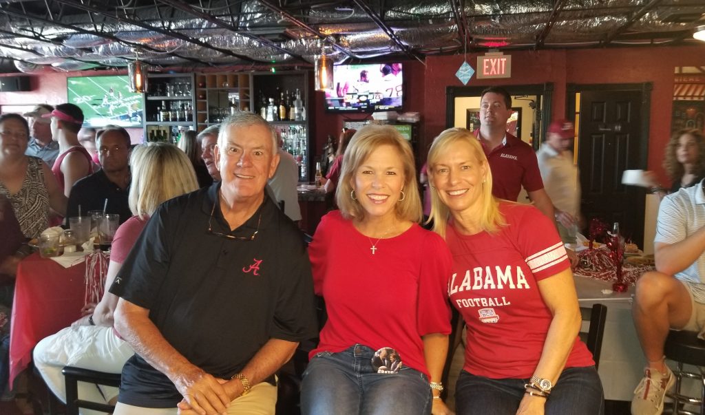 Man in black shirt and to women in red shirts sitting in front of dark wall