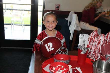 Child standing in front of Alabama helment with number 12 in front of window.