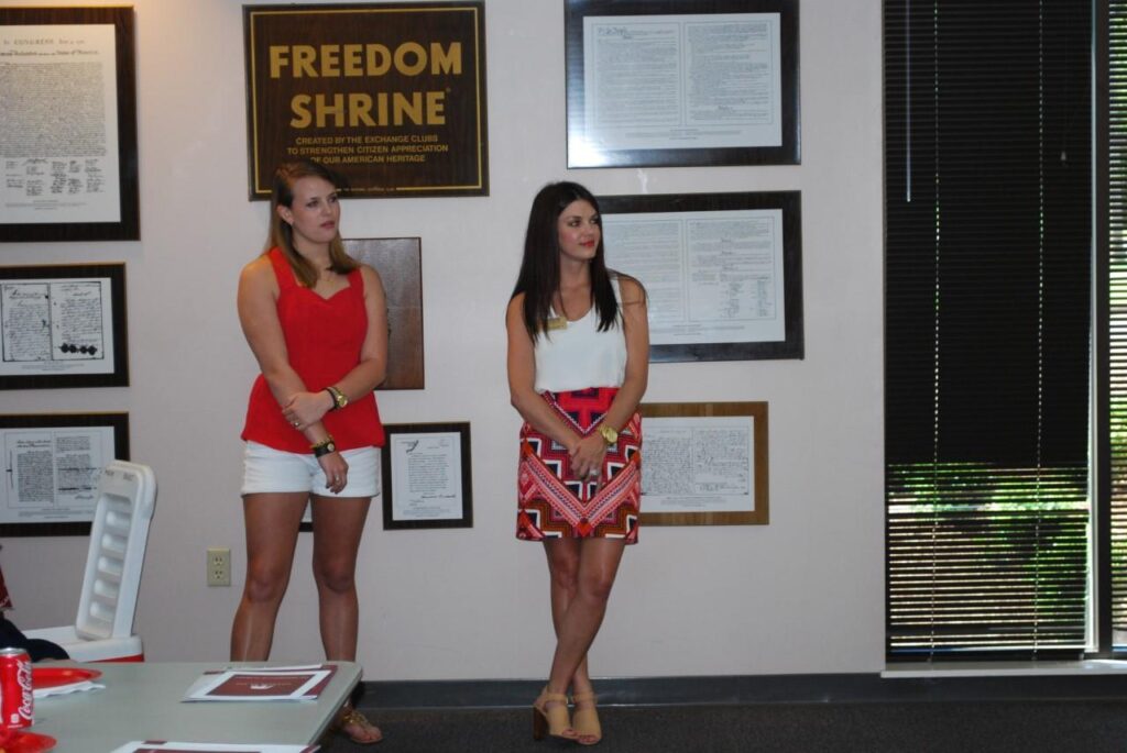 Two students standing in front of white wall with pictures on wall.