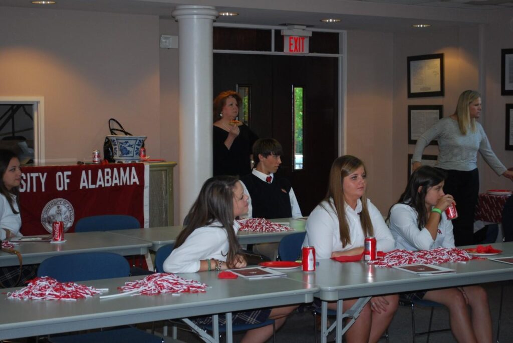 Group of students sitting behind table in front of white column and brown door.