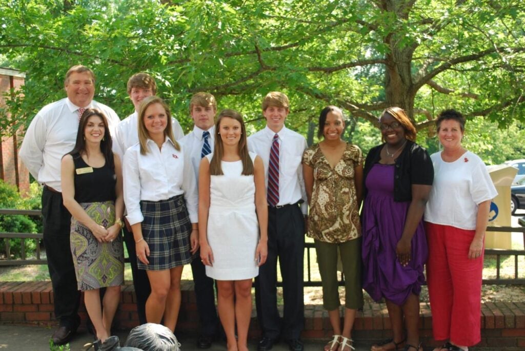 Group of students standing outside with green trees in background.