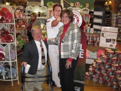 Terry Saban standing next to Nick Saban poster and man in blue jacket.