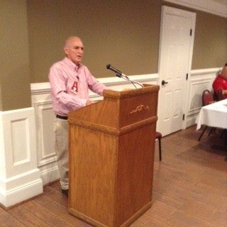Ma in red shirt standing behind a podium