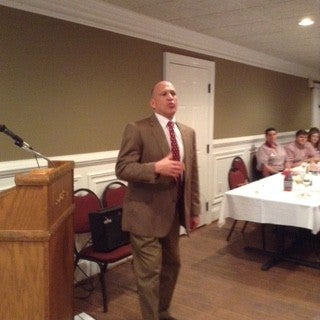 Man in brown suit standing in front of a podium.