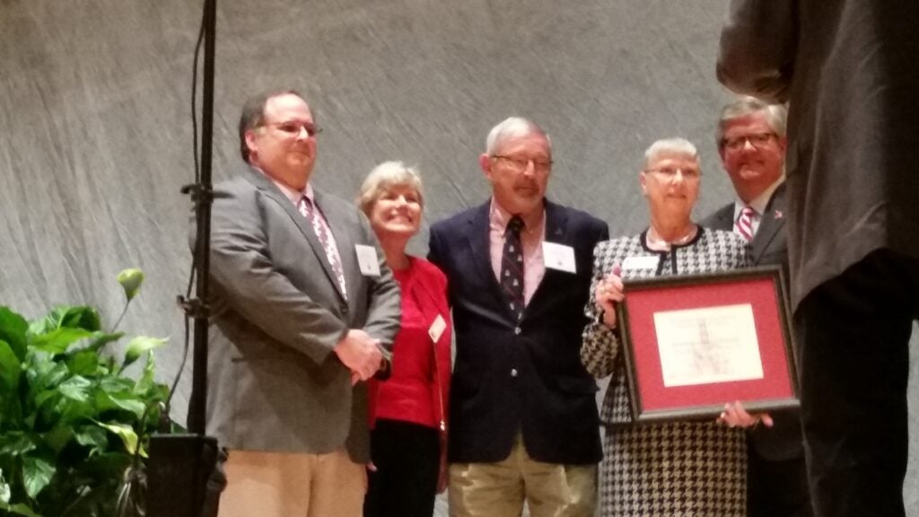 Four people standing in front of gray wall.
