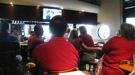People sitting at table watching TV Screen.