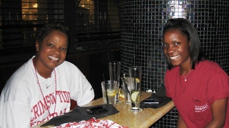 Two ladies sitting at table with black wall.