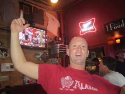 Man in a red shirt standing in a bar.