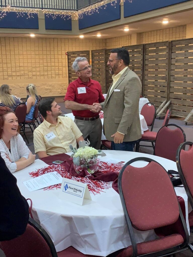 group of people sitting at table and two men standing in front of dark wall