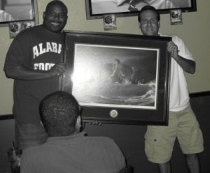 Black and white photo of two men holding picture in frame.
