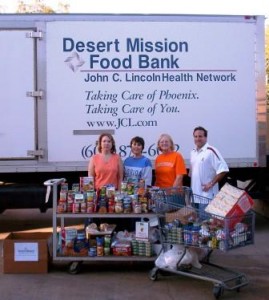 Group of people standing behind boxed food on cart and food bank sign in background.