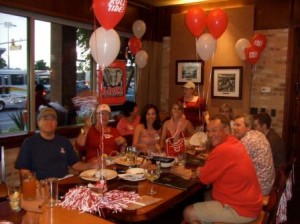 Group of people sitting at table with red and white balloons.