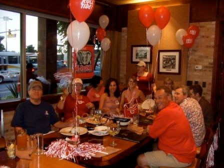 Group of people sitting at table with red and white balloons.