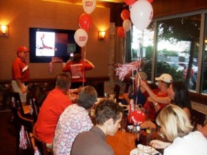 Group of people sitting in room with balloons on table. TV screen in background.