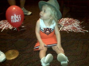 Little girl dressed in white and orange dress with houndstooth hat.