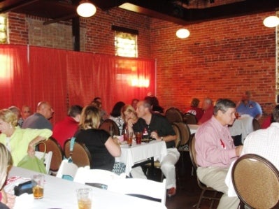 Group of people sitting at table in room with red background.