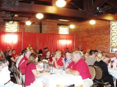 Group of people sitting at table with red curtain in background.
