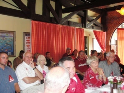 Group of people sitting at table in room with red curtain in background.