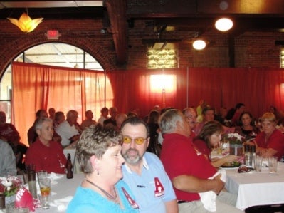 Group of people sitting at table in room with red curtain background.