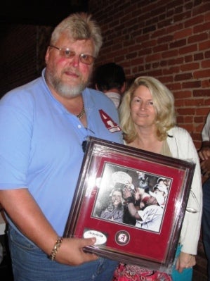 Man in Blue Shirt and lady in white sweater holder a framed picture.
