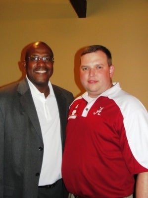 Two people standing in front of brown wall.