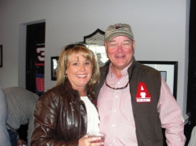 Two people standing in front of white wall.