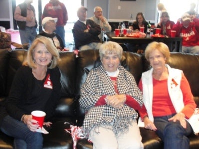 Three people sitting and people standing in the background.