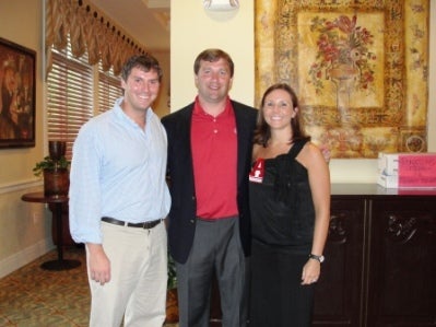 three people standing in room in front of beige wall.