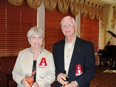 Women in White jacket and man in black jacket standing in front of window with brown shades.