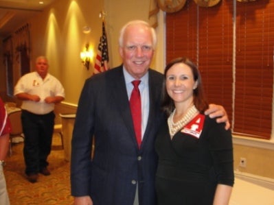 Man in black jacket and red tie standing by lady in black dress.
