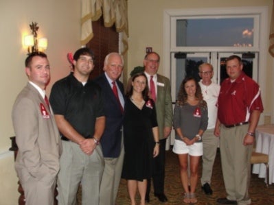 Group of people standing in room with white wall in background.