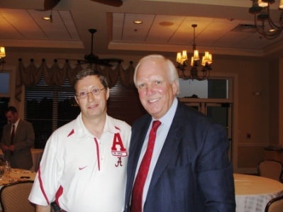 Man in white shirt and man in black jacket standing in room with dim light.