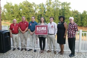 Group of people standing outside one in middle holding a red and white BAMA Bound sign.