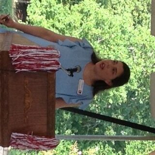 Girl in blue dress standing behind podium outside.