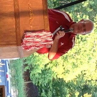 Man in red shirt standing behind podium outside.