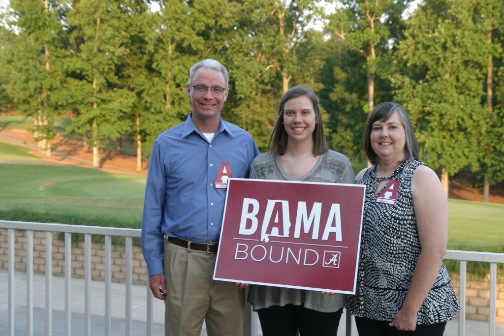 Three people standing outside and one holding a BAMA Bound sign.