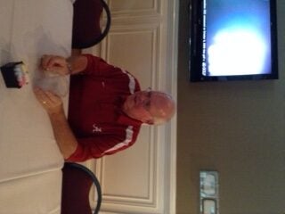 Man in red shirt sitting at a table with white wall in background.