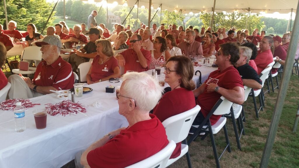Group of people sitting at table outside under a tent.