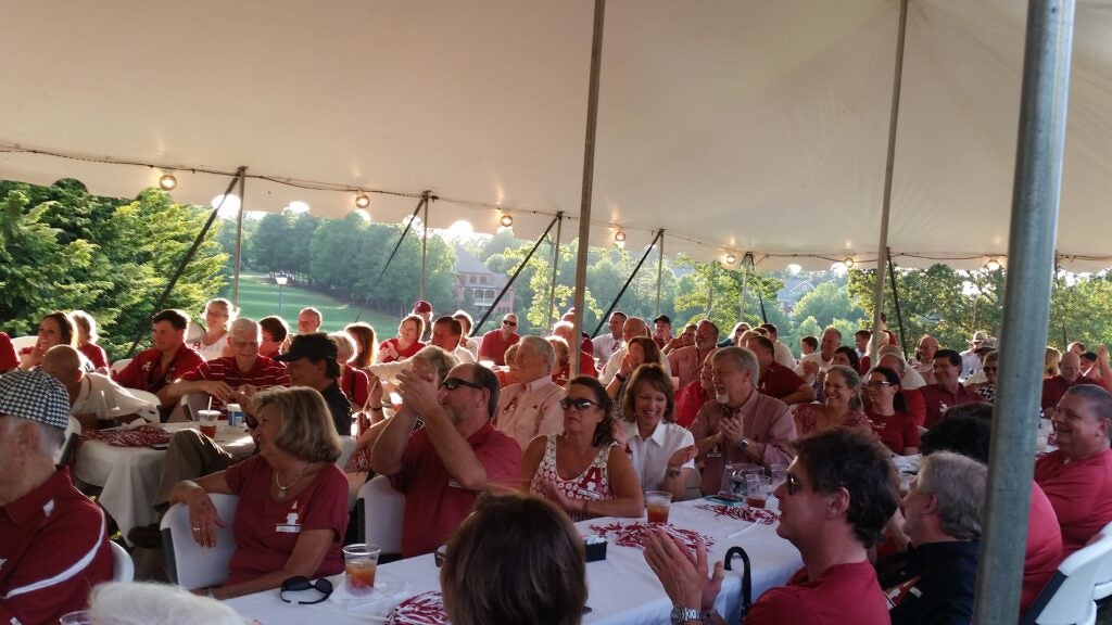 Group of people sitting at table outside under a tent.