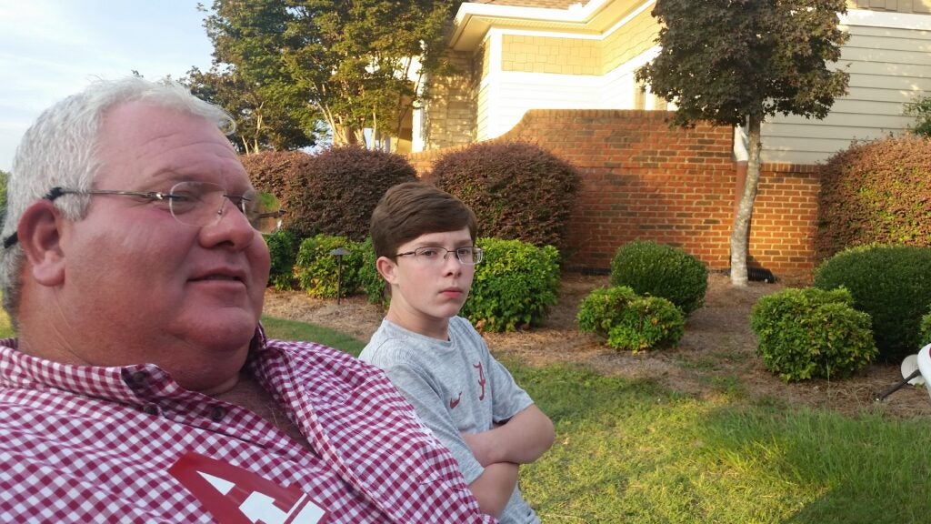 Two people standing outside in front of brick wall.