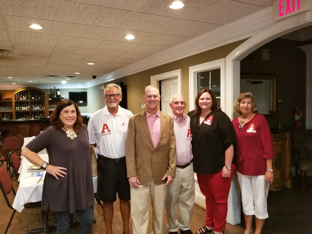 Group of people standing in room with beige and white background.
