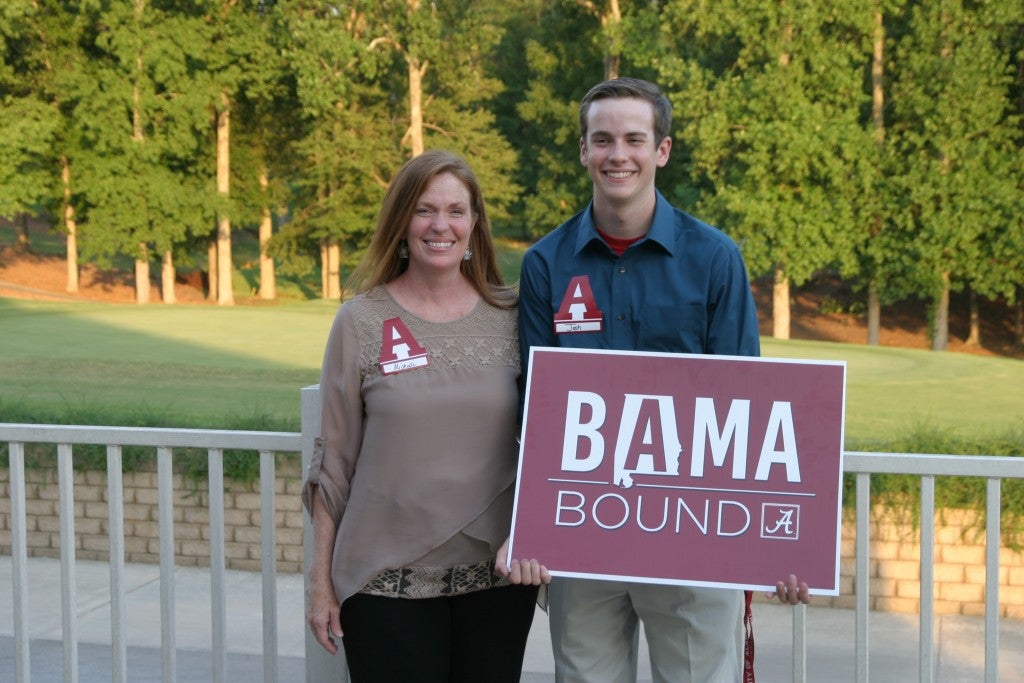 Two people standing outside holding a red and white BAMA Bound sign.