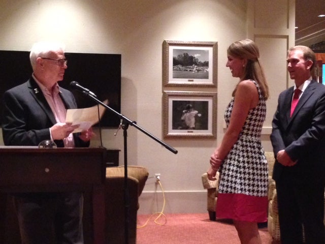 Man standing behind podium and girl in black/white dress standing in front of white wall.