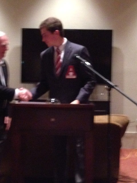 Man standing behind podium in dark suite in front of black/white wall.